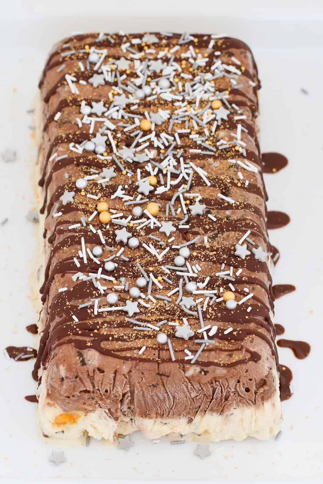 Gold and silver sprinkles and chocolate sauce over a chocolate and vanilla ice-cream cake.