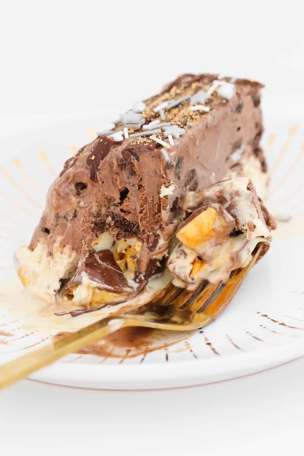 Chunks of honeycomb on a fork in front of a slice of chocolate ice-cream cake.