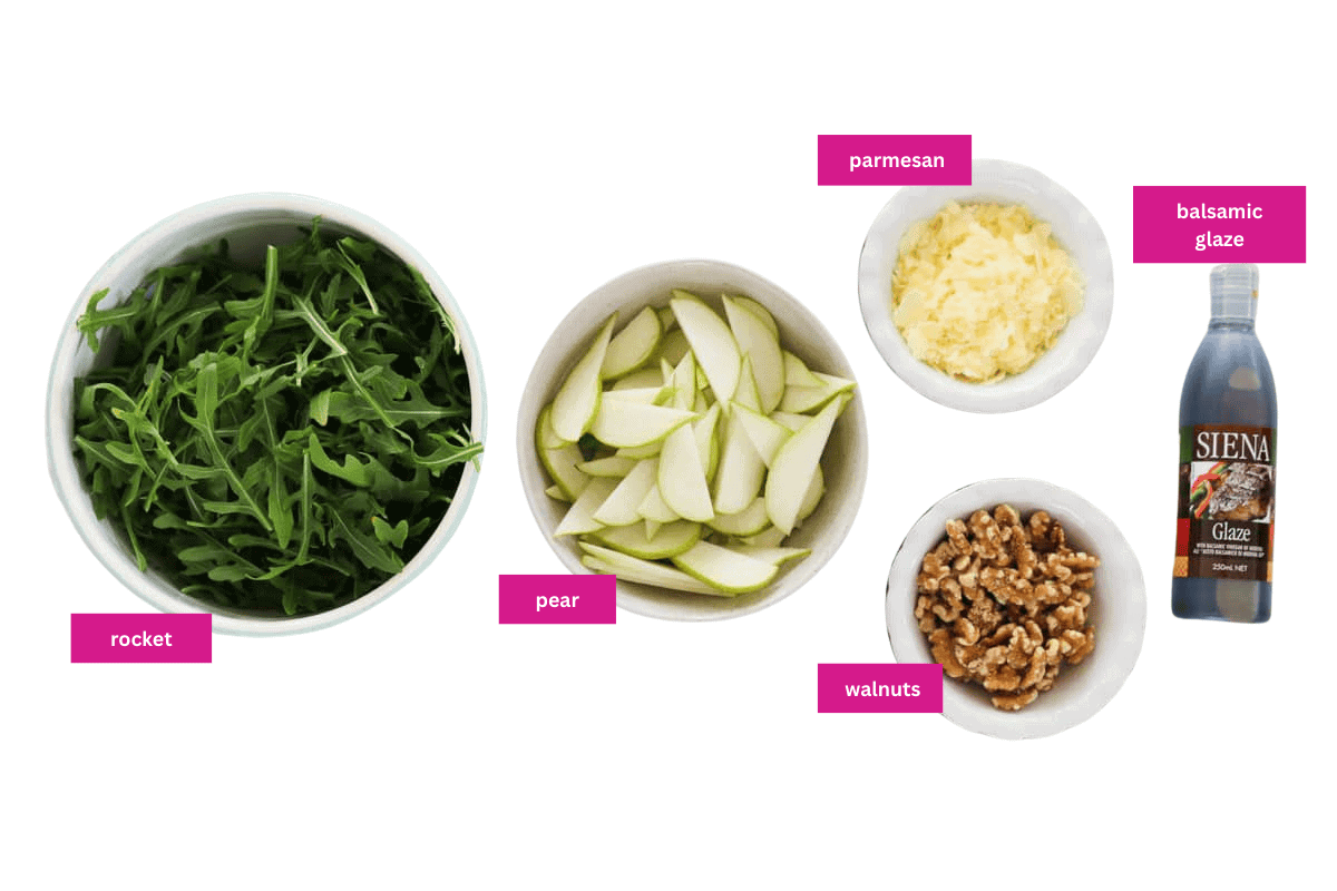 Rocket, sliced pear, parmesan, walnuts and balsamic glaze laid out on a white background.