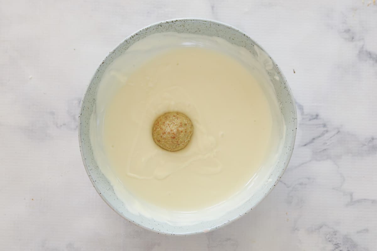 A cheesecake ball being dipped into a bowl of melted white chocolate.