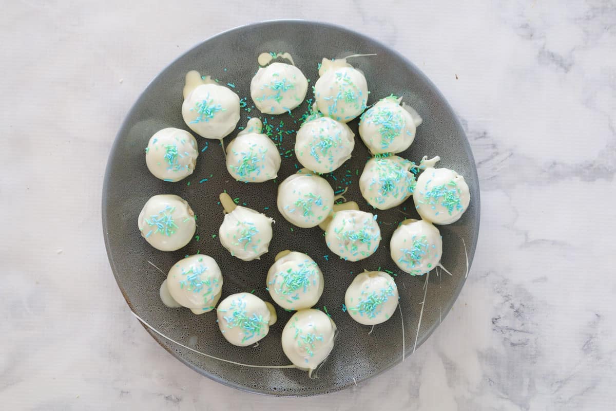 White chocolate cheesecake balls with green sprinkles on a plate.