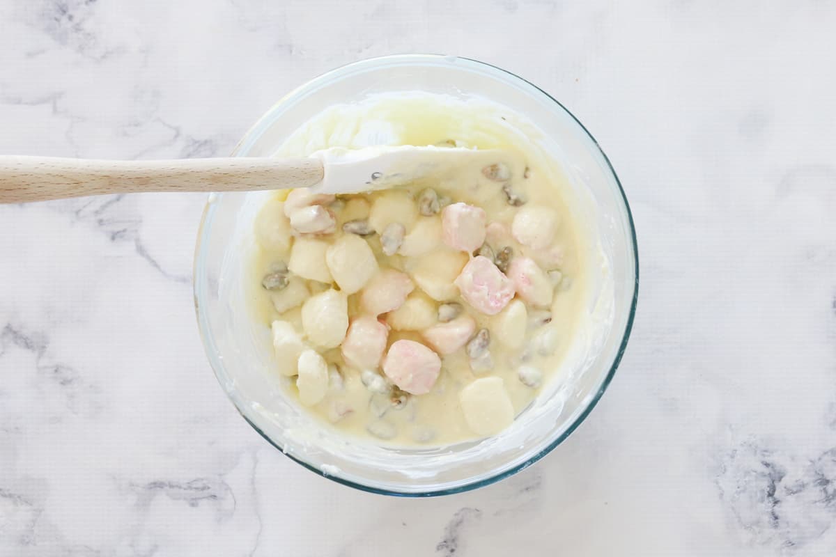 A spatula mixing together a bowl of melted white chocolate, marshmallows, Turkish Delight and pistachios.