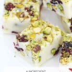 A Pinterest image of pieces of white chocolate Christmas fudge with pistachios and cranberries.