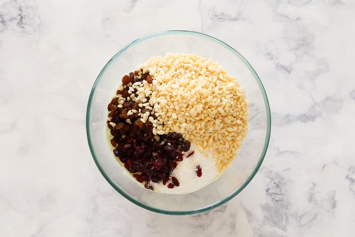 Rice bubbles, dried cranberries, sultanas, almonds, coconut and melted white chocolate in a bowl.