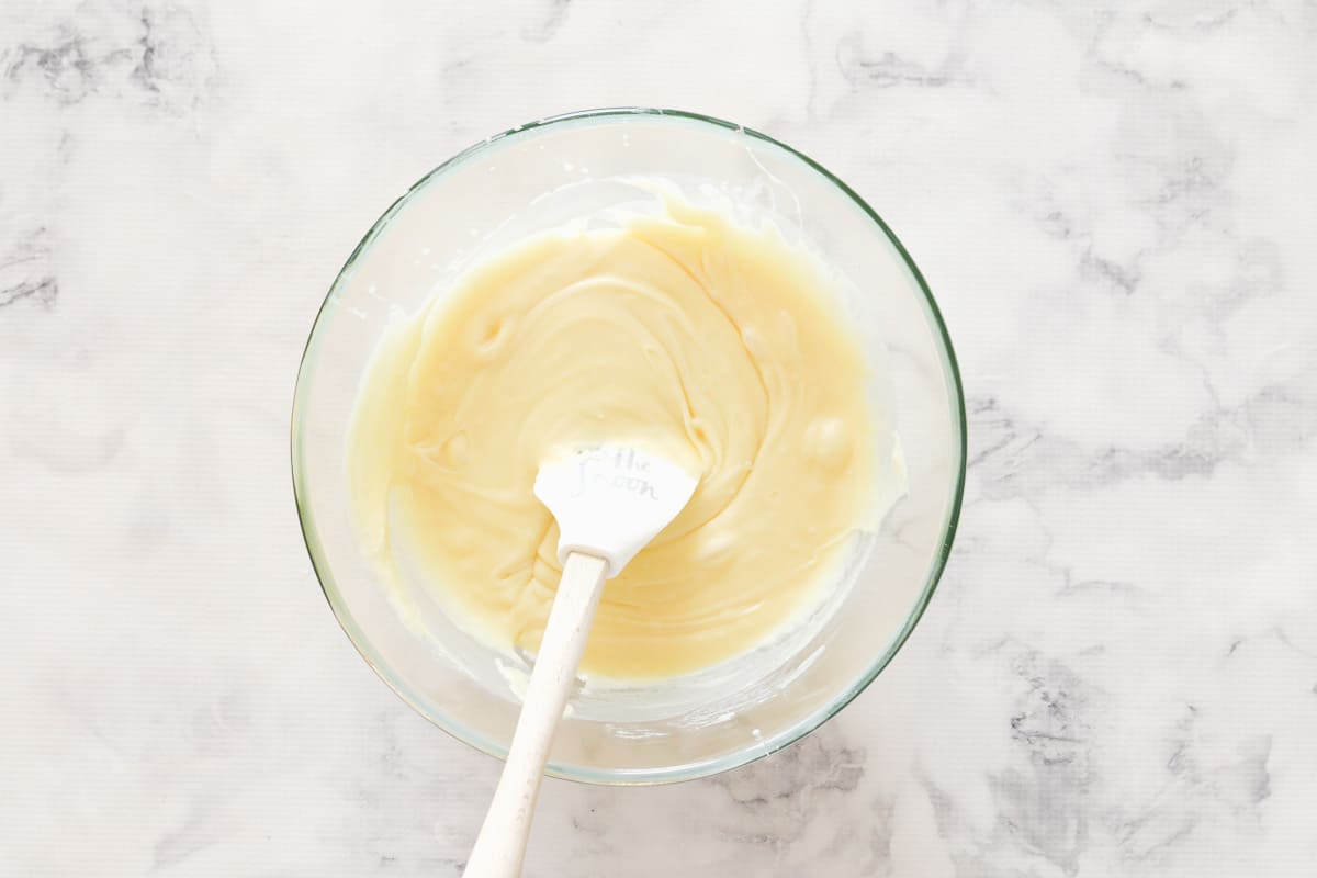 A spatula mixing melted white chocolate and condensed milk in a bowl