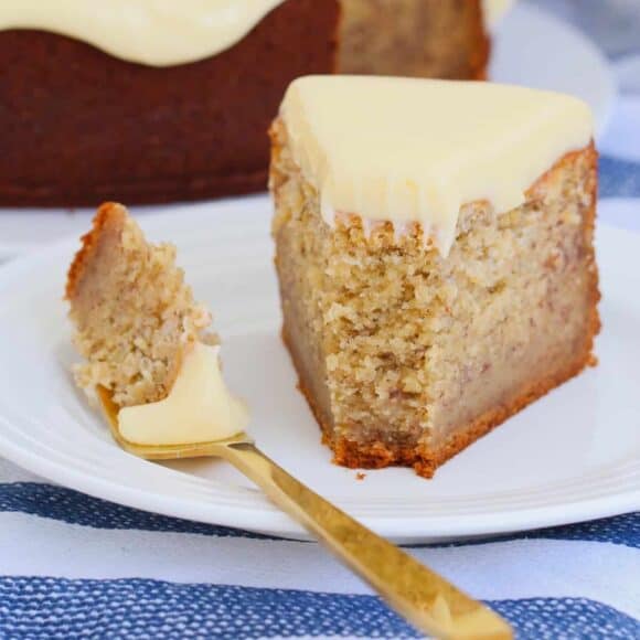 A slice of banana cake with cream cheese frosting on a plate.