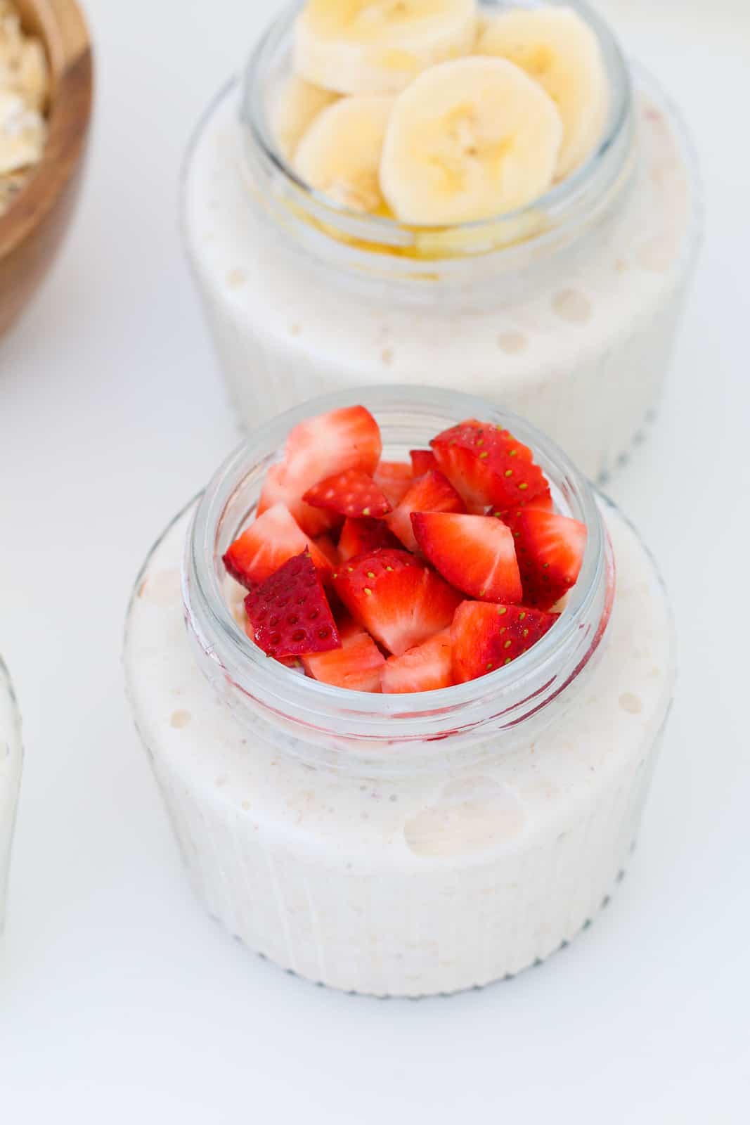 Strawberries on top of a small glass jar filled with bircher muesli.