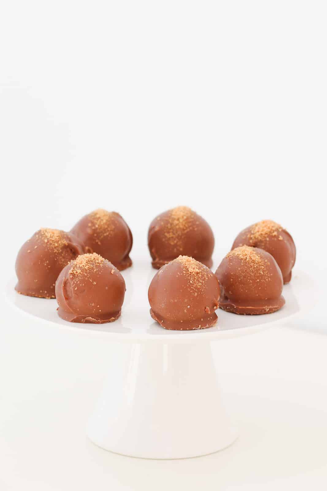A plate of milk chocolate coated caramel Tim Tam cheesecake balls with gold sugar sprinkled on top.