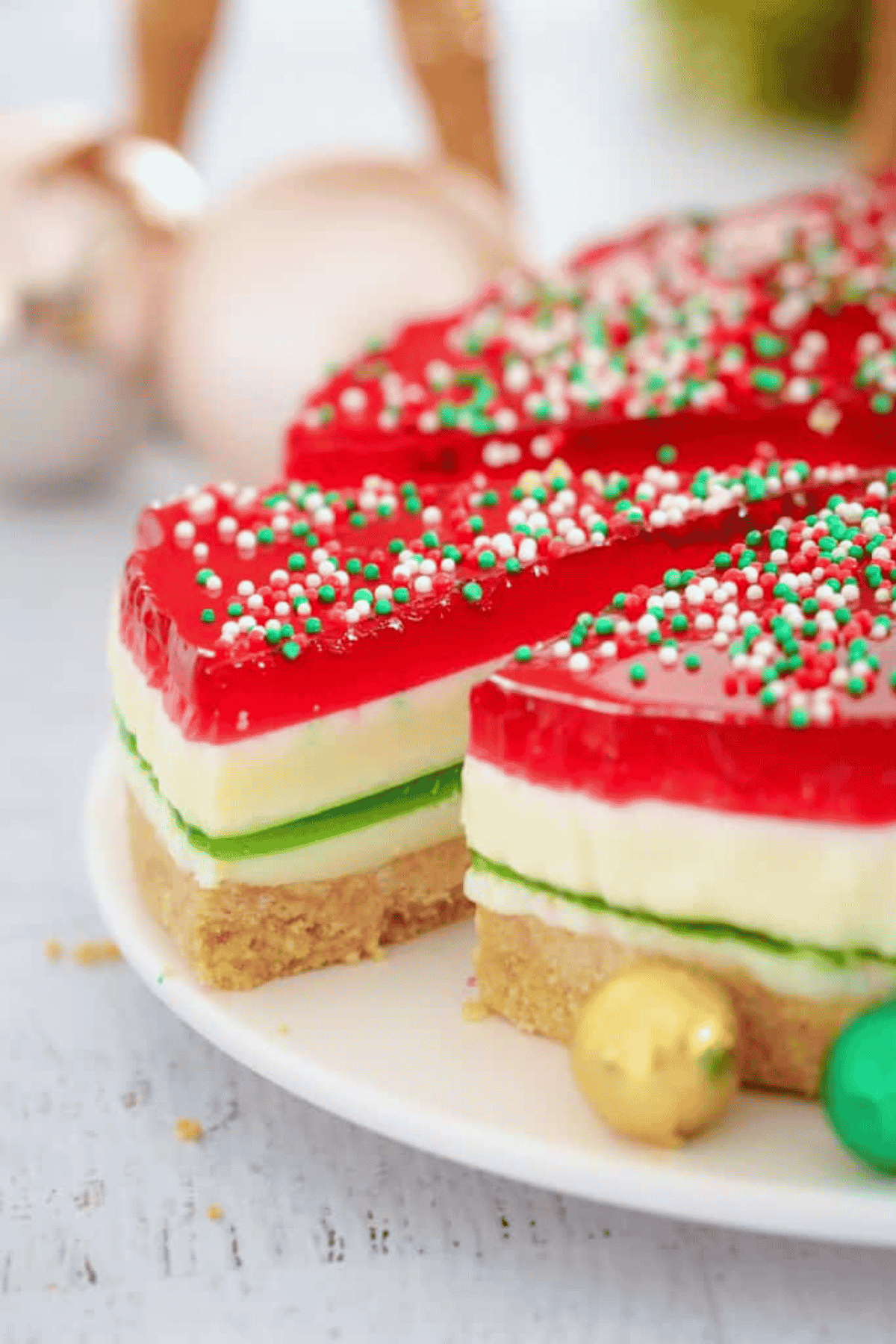 A Christmas coloured jelly cake with a biscuit base and a slice being removed.