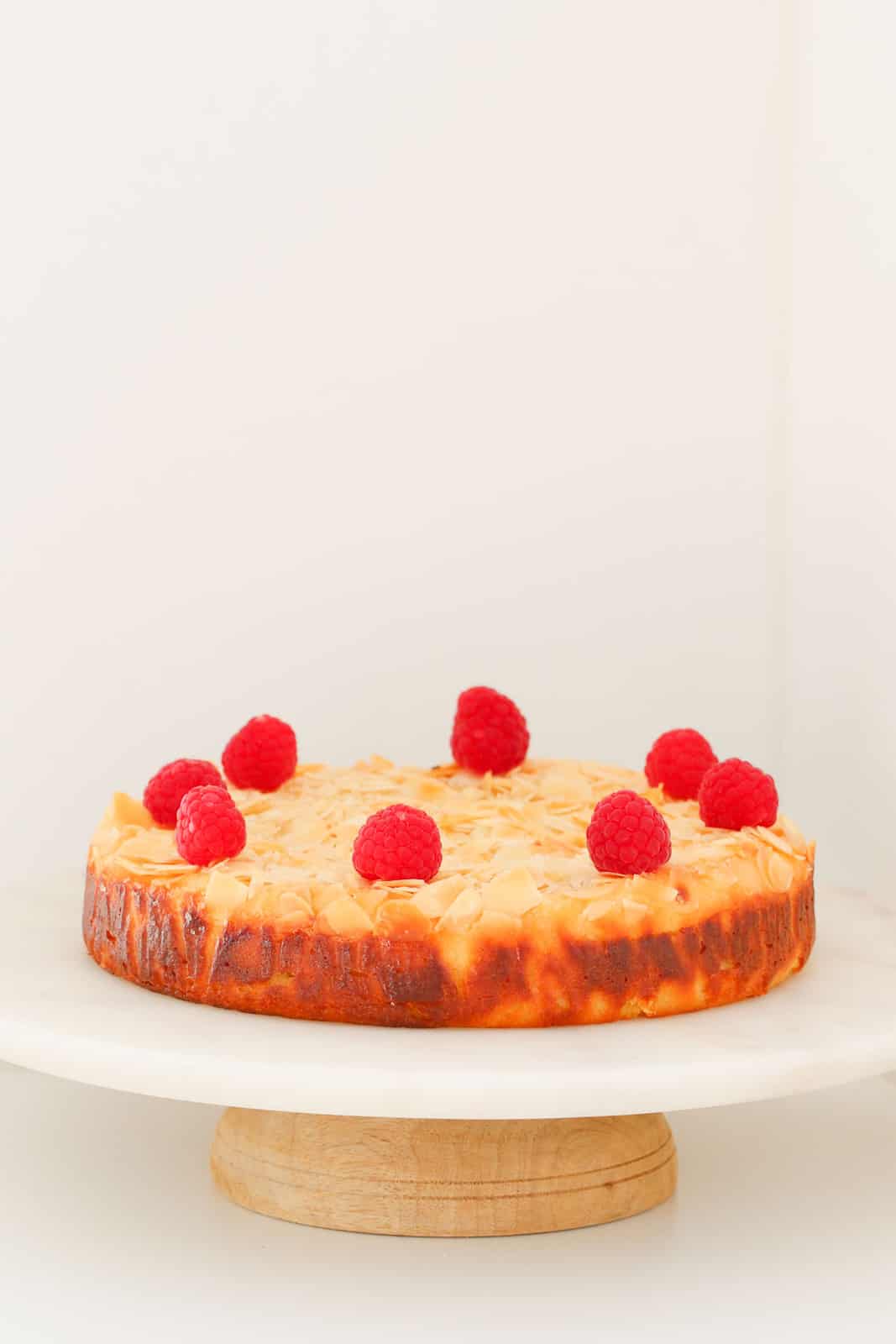 Lemon & Ricotta cake decorated with raspberries on a white cake stand
