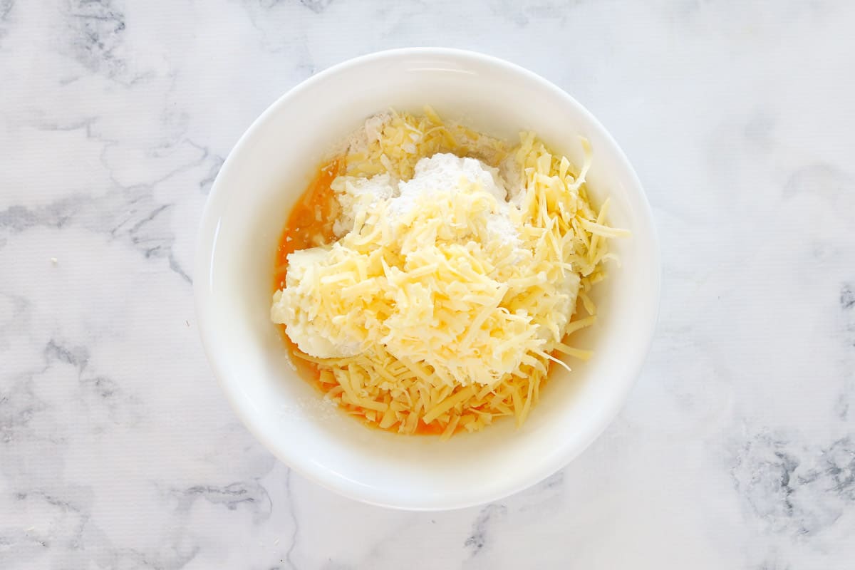 Mashed potato, grated cheese and egg in a white bowl.
