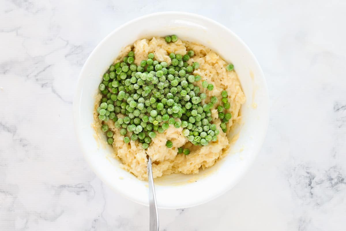 Peas on top of mashed potato in a white bowl.