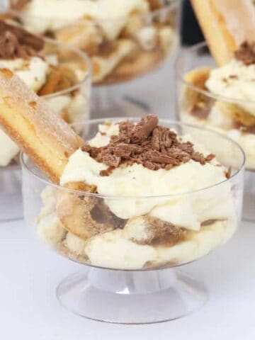 Small glass bowls filled with cream, shaved chocolate, Kahlua and sponge finger biscuits.