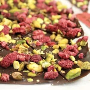 Dark chocolate bark with pistachios and dried raspberries being cut up on a board.