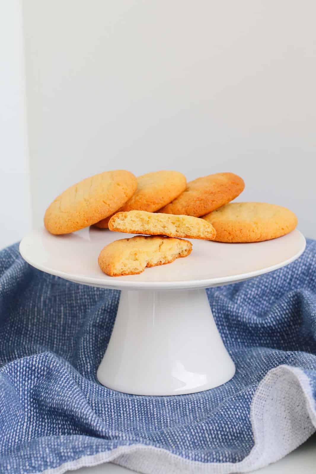 A white cake stand with honey cookies and one broken in half.