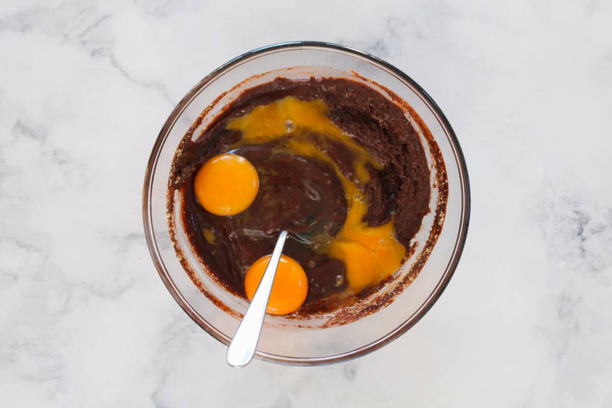 Brownie mix with two eggs and one egg yolk, in a glass mixing bowl.