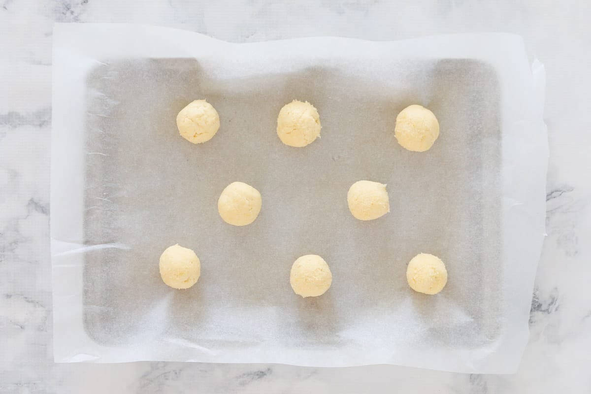 Eight spoonfuls of biscuit dough on a paper lined baking tray.