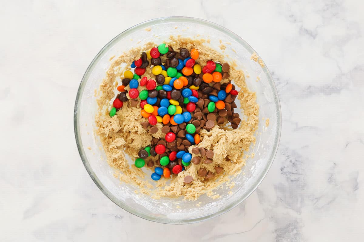 M&M's and chocolate chips added to cake batter in glass mixing bowl.