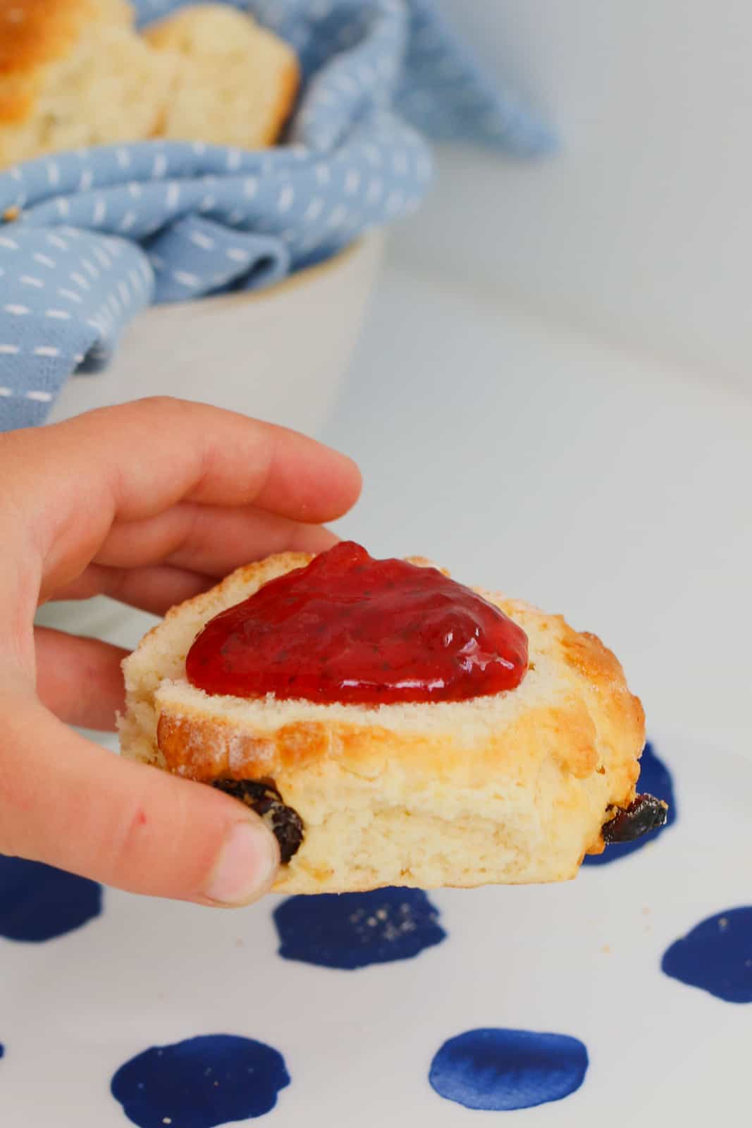 A close up shot of a hand holding a fruit scone with red jam on top