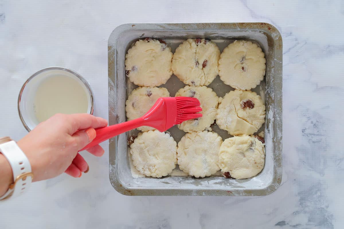 Fruit scones in a baking tin being brushed with milk