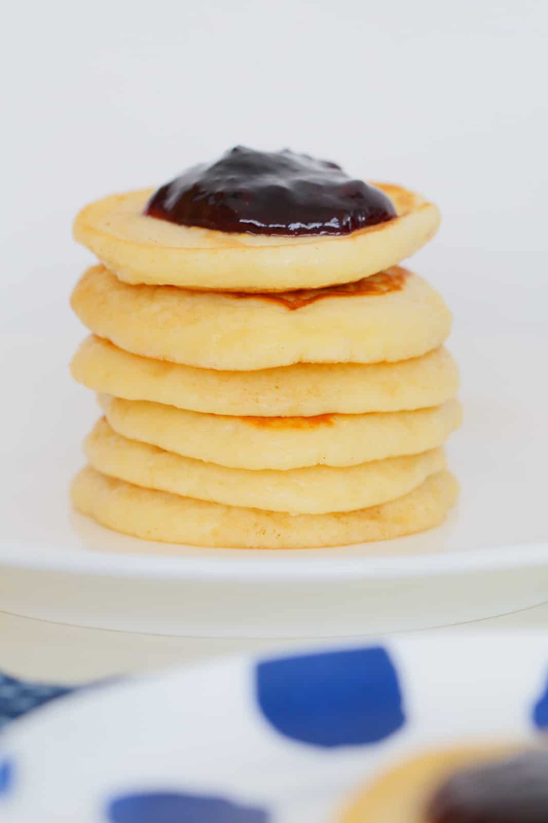 A stack of pikelets on a white stand with a dollop of jam on top.