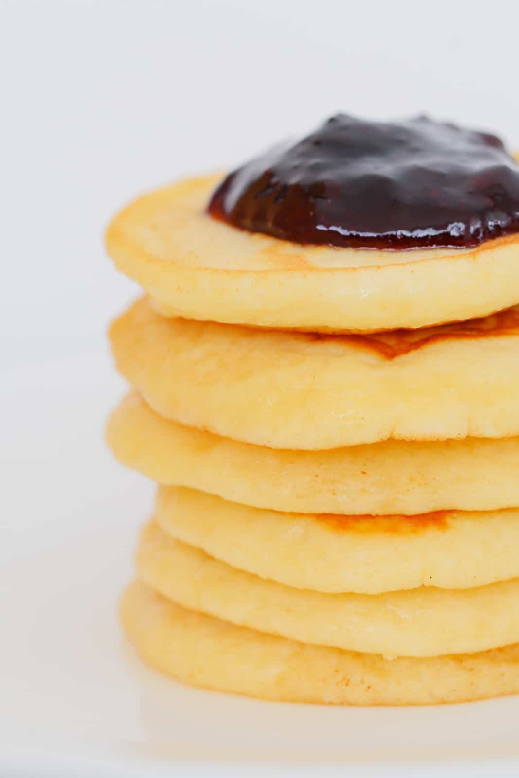 A close up of a pile of small sweet round pikelets with jam on the top one.