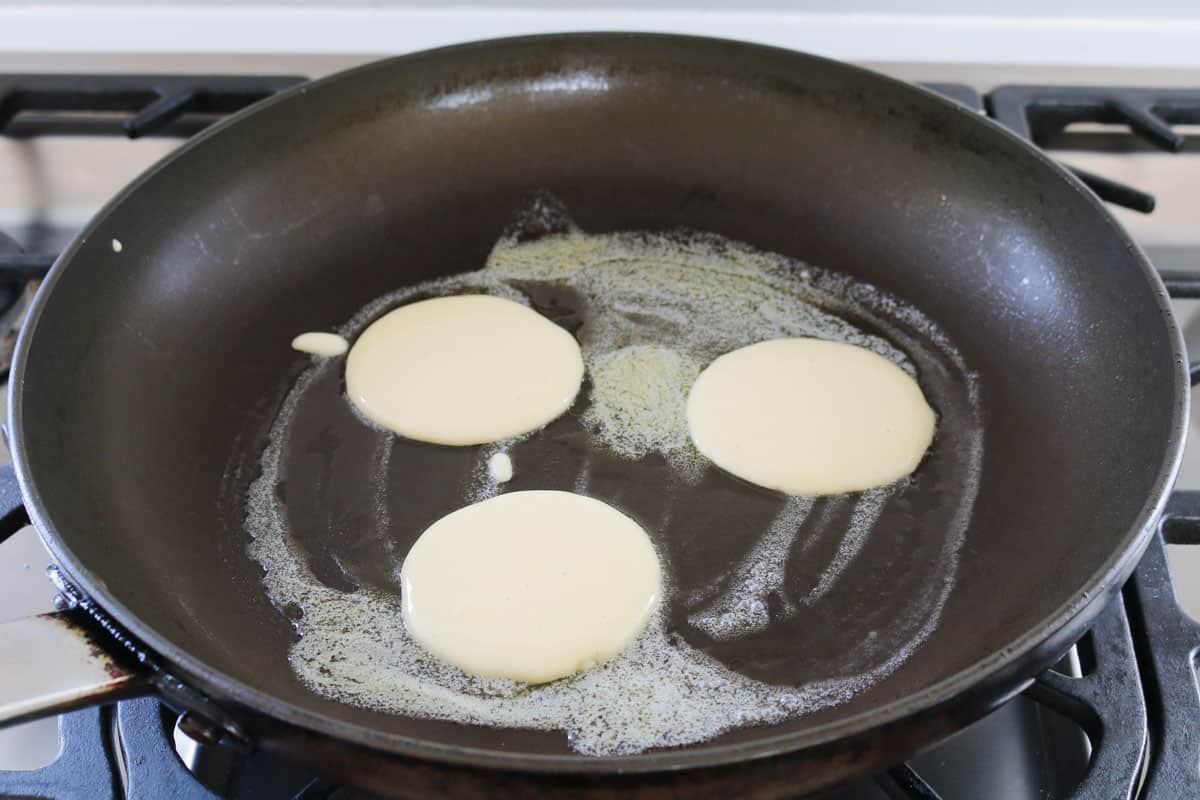 Pikelet batter cooking in a frying pan.