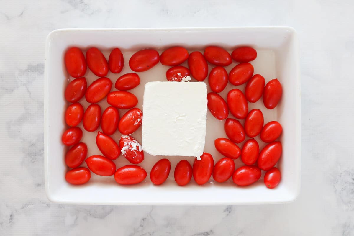 A block of feta and cherry tomatoes in a baking dish.