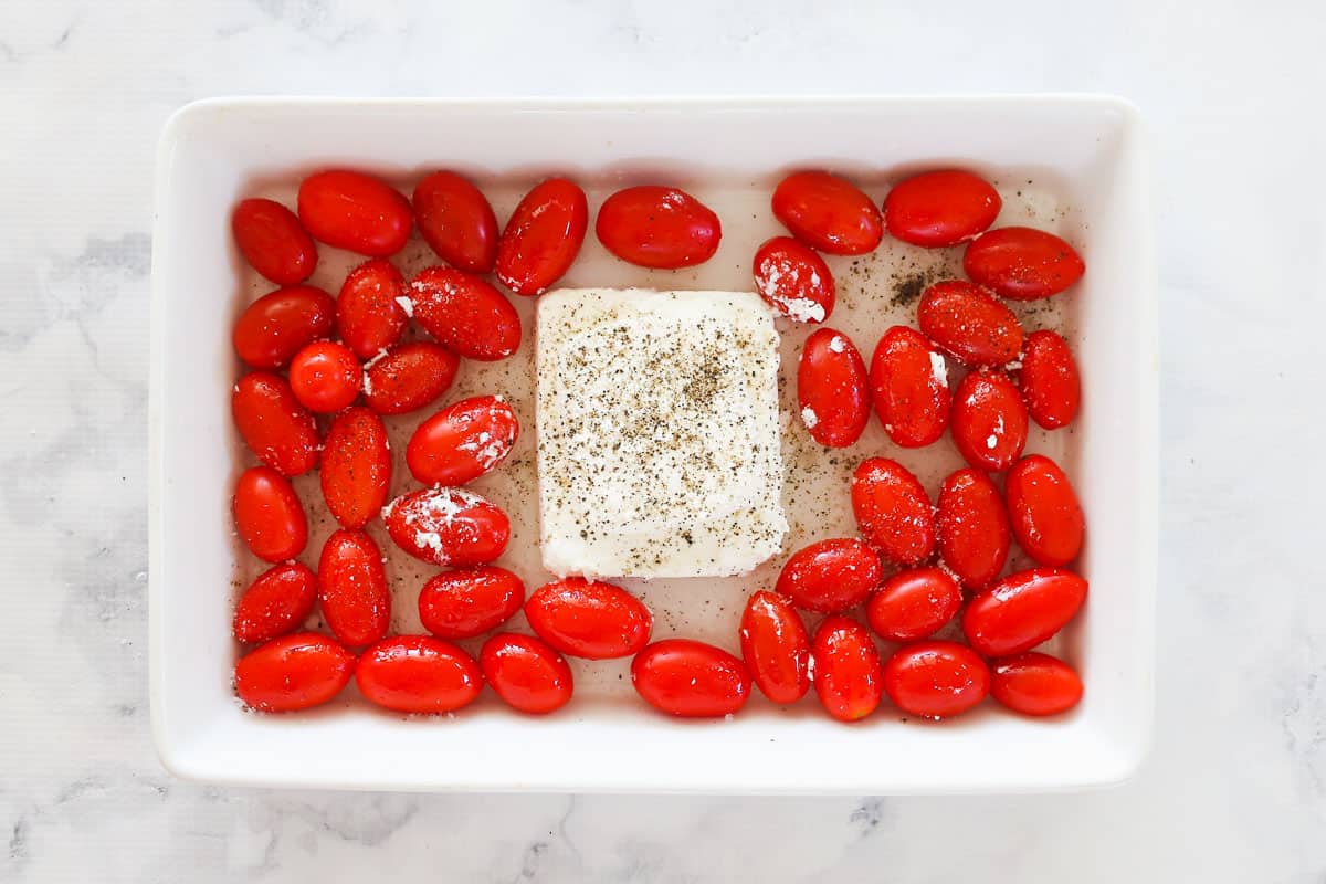 Feta and tomatoes seasoned with salt and pepper in a baking dish.