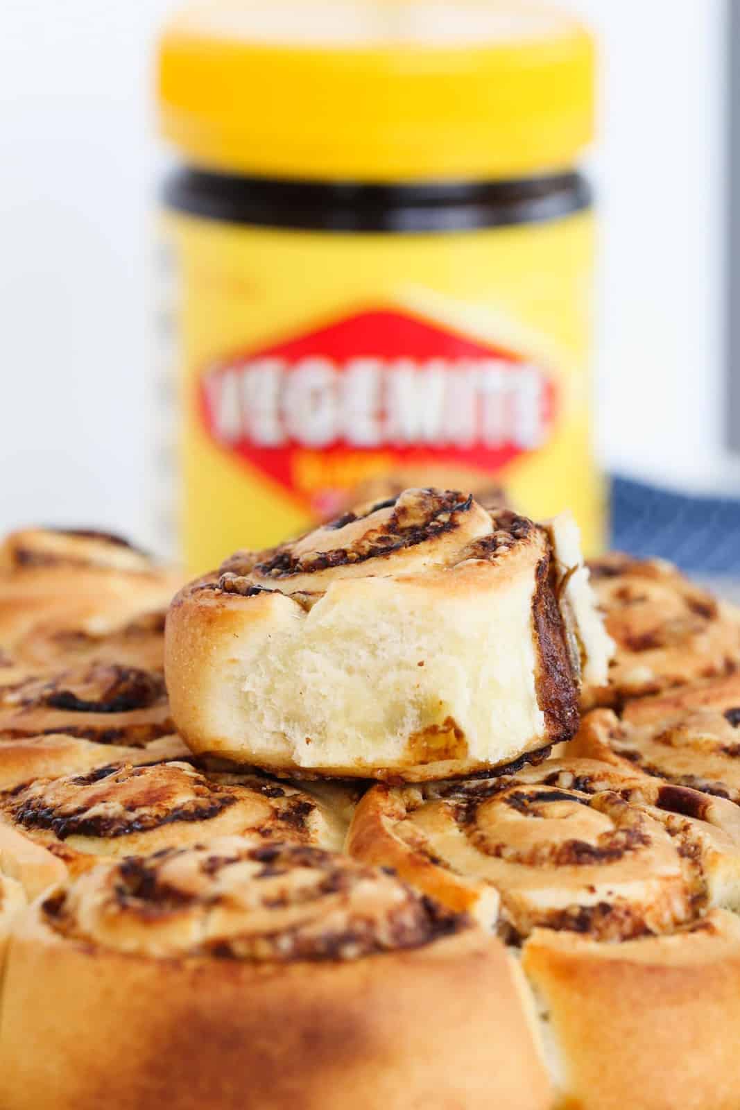 A baked scroll with a vegemite and cheese filling sitting on top of a layer of scrolls in front of a Vegemite jar.