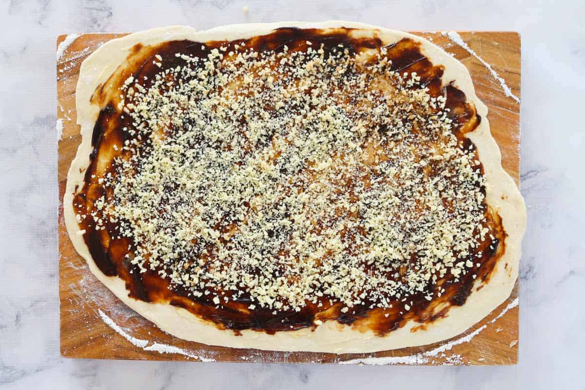 Dough rolled out on a wooden board, spread with Vegemite and sprinkled with grated cheese.