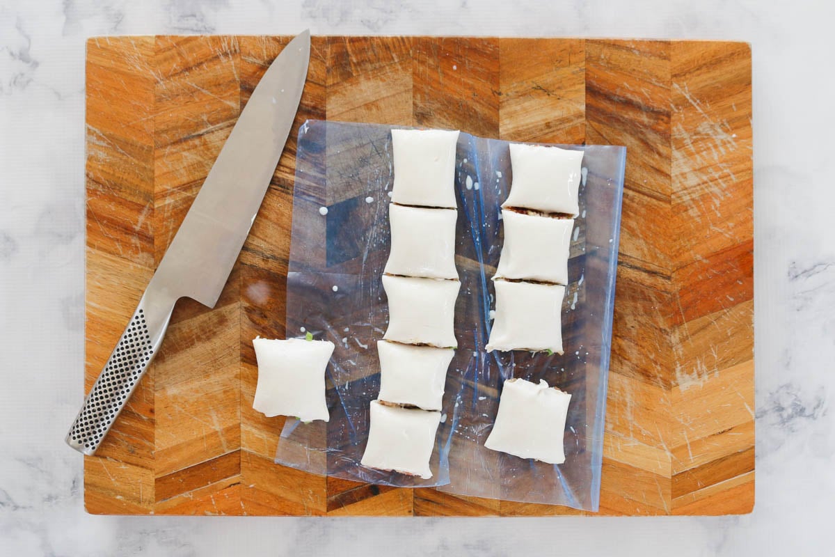 Pastry rolls being cut into pieces on a wooden chopping board.