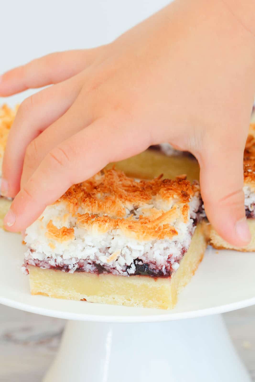 A child's hand picking up a piece of Raspberry Coconut Slice.