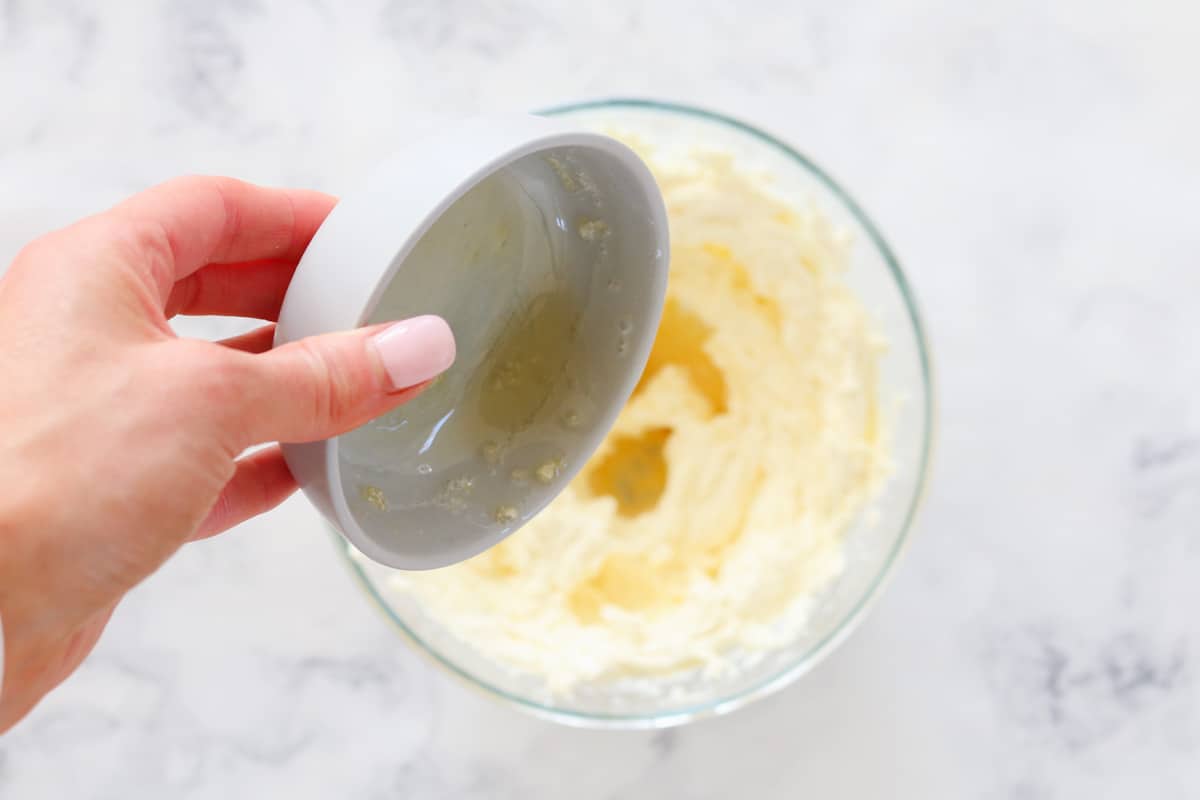 Dissolved gelatine being added to a bowl of cheesecake mixture.