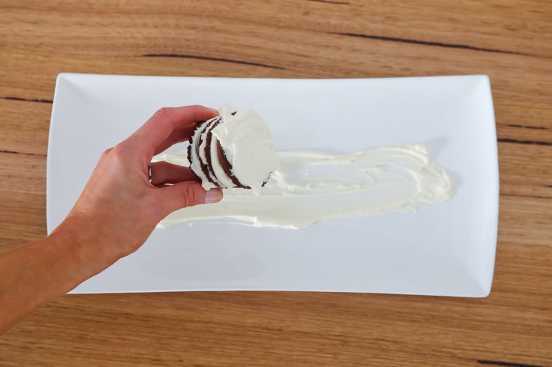 A hand holding chocolate biscuits coated in whipped cream.