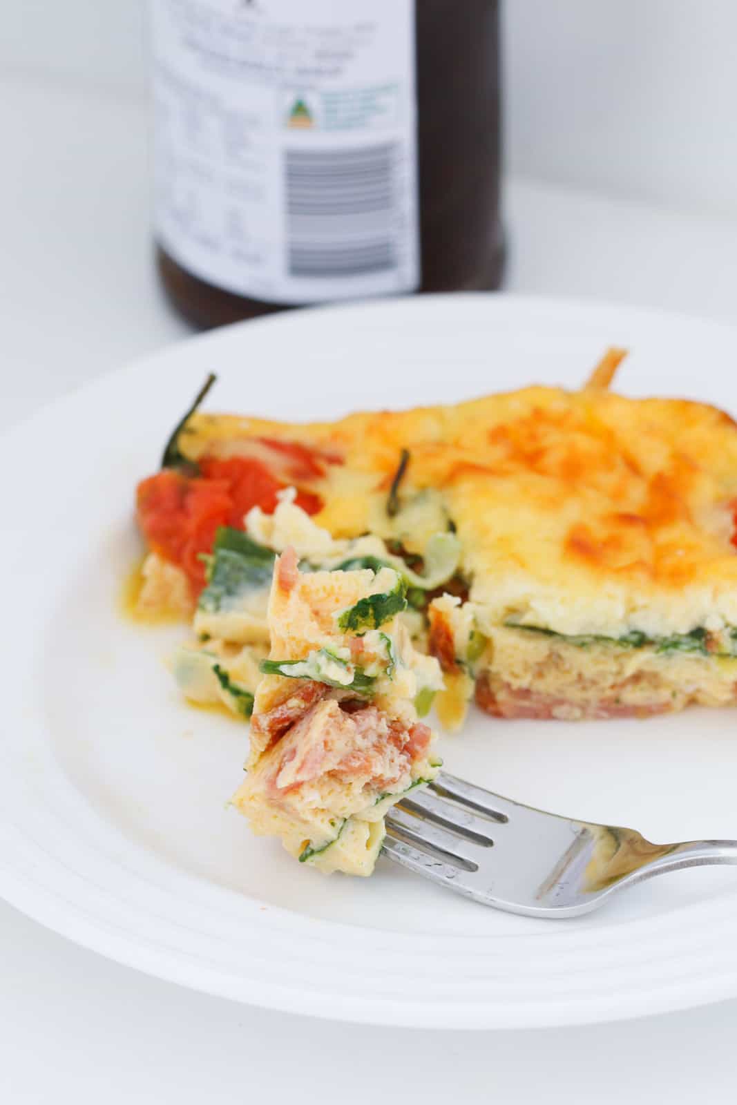 A plate of a savoury bacon, spinach and tomato frittata, with some on a fork.