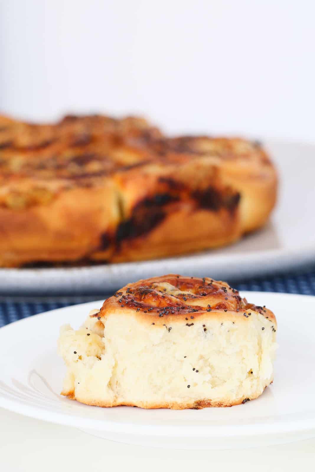 A fluffy white scroll on a plate with a golden top and poppyseeds sprinkled over.