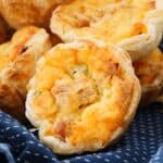 Individual serve quiches with a puff pastry crust arranged on a blue patterned tea towel.