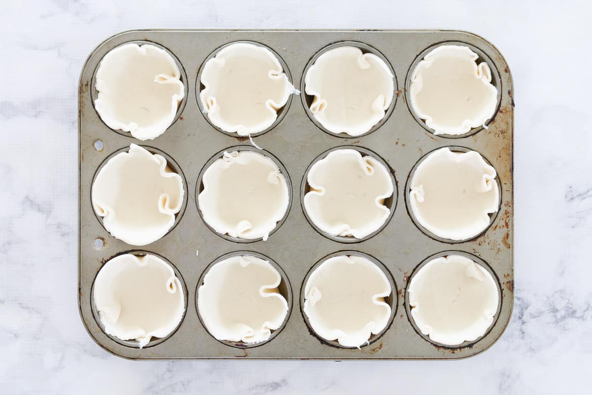 A 12-hole muffin tin with puff pastry circles lining the holes, on a marble countertop