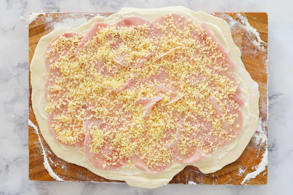 Layers of shaved deli ham and grated cheese on scroll dough.