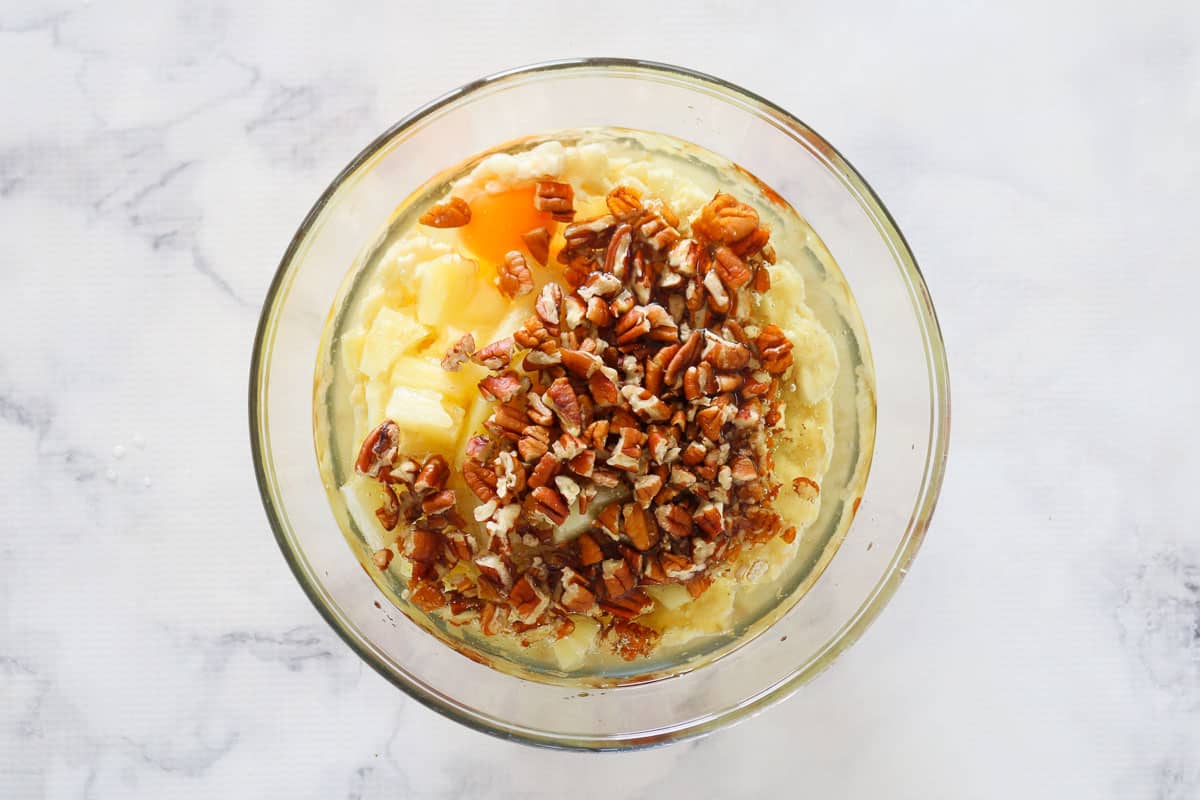 Mashed bananas, chopped pineapple, oil, eggs and pecans in a bowl.