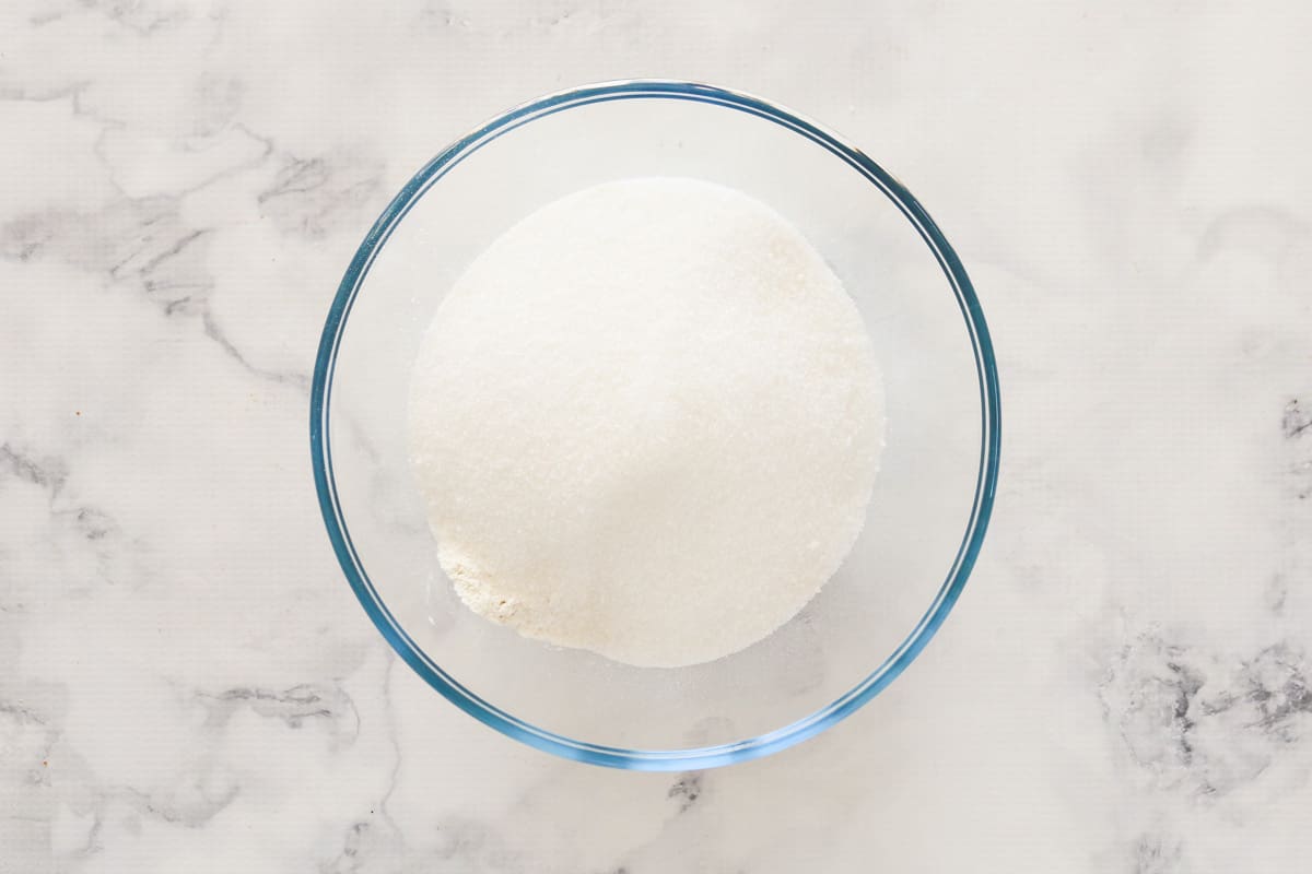 Flour and baking powder in a glass bowl on a marble bench.