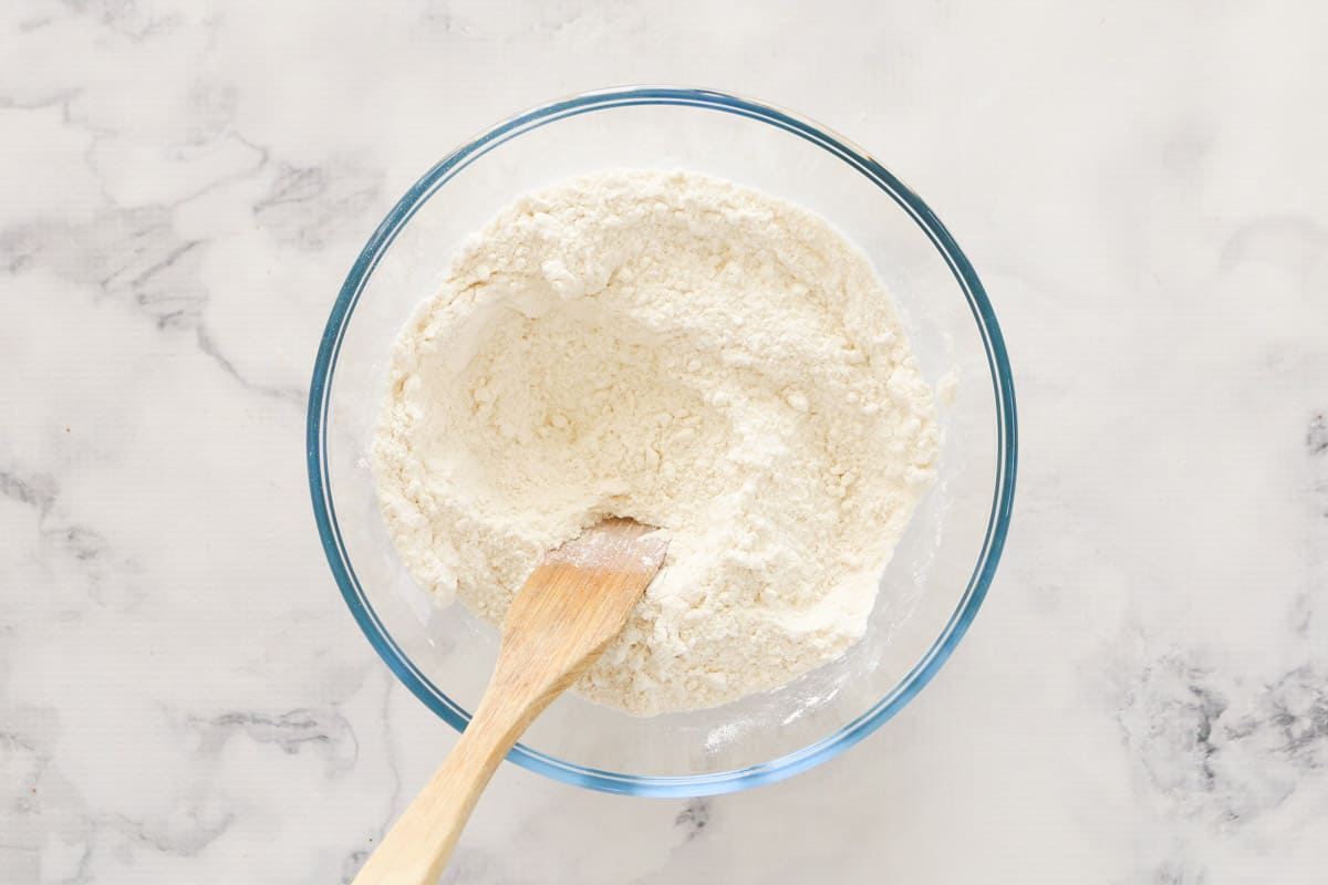 Sugar and salt added to flour in a clear bowl with wooden spoon