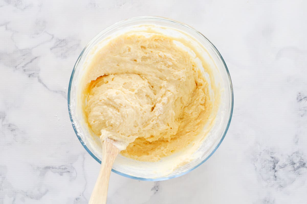 Top view of ricotta cake batter in clear bowl with wooden spoon
