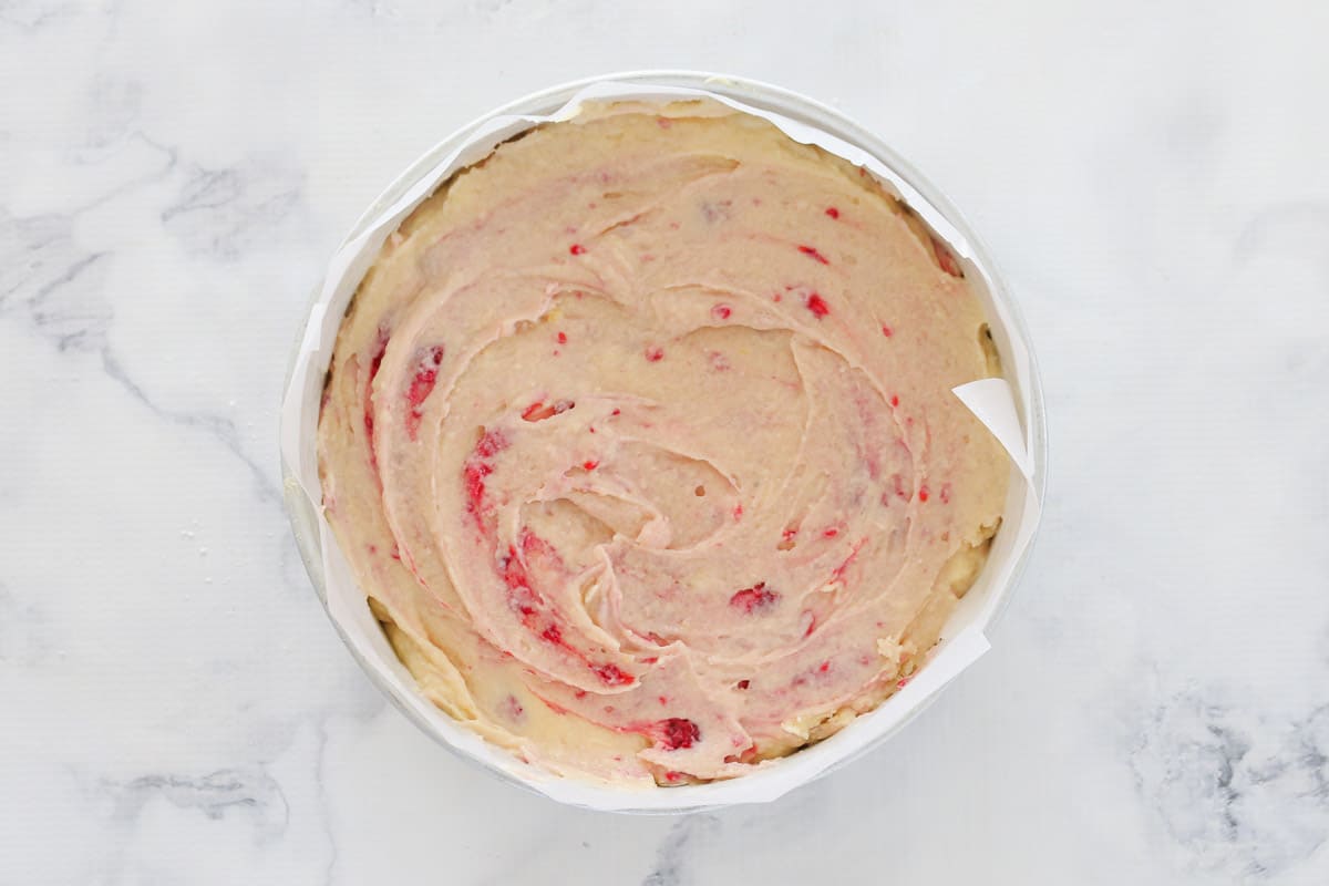 Cake batter with raspberries folded through in a spring-form tin.