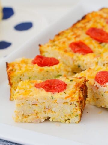 A vegetable egg and ham slice cut into pieces with cherry tomatoes on top.