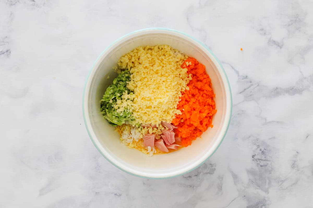 Grated vegetables, cheese and ham over an egg and rice mixture in a bowl.