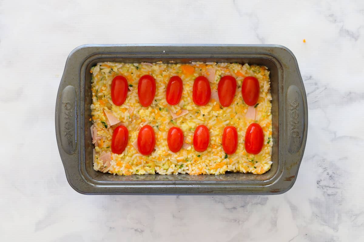 Cherry tomatoes decorating a unbaked savoury slice in a loaf tin.