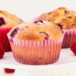 A muffin studded with raspberries in a pink muffin liner.