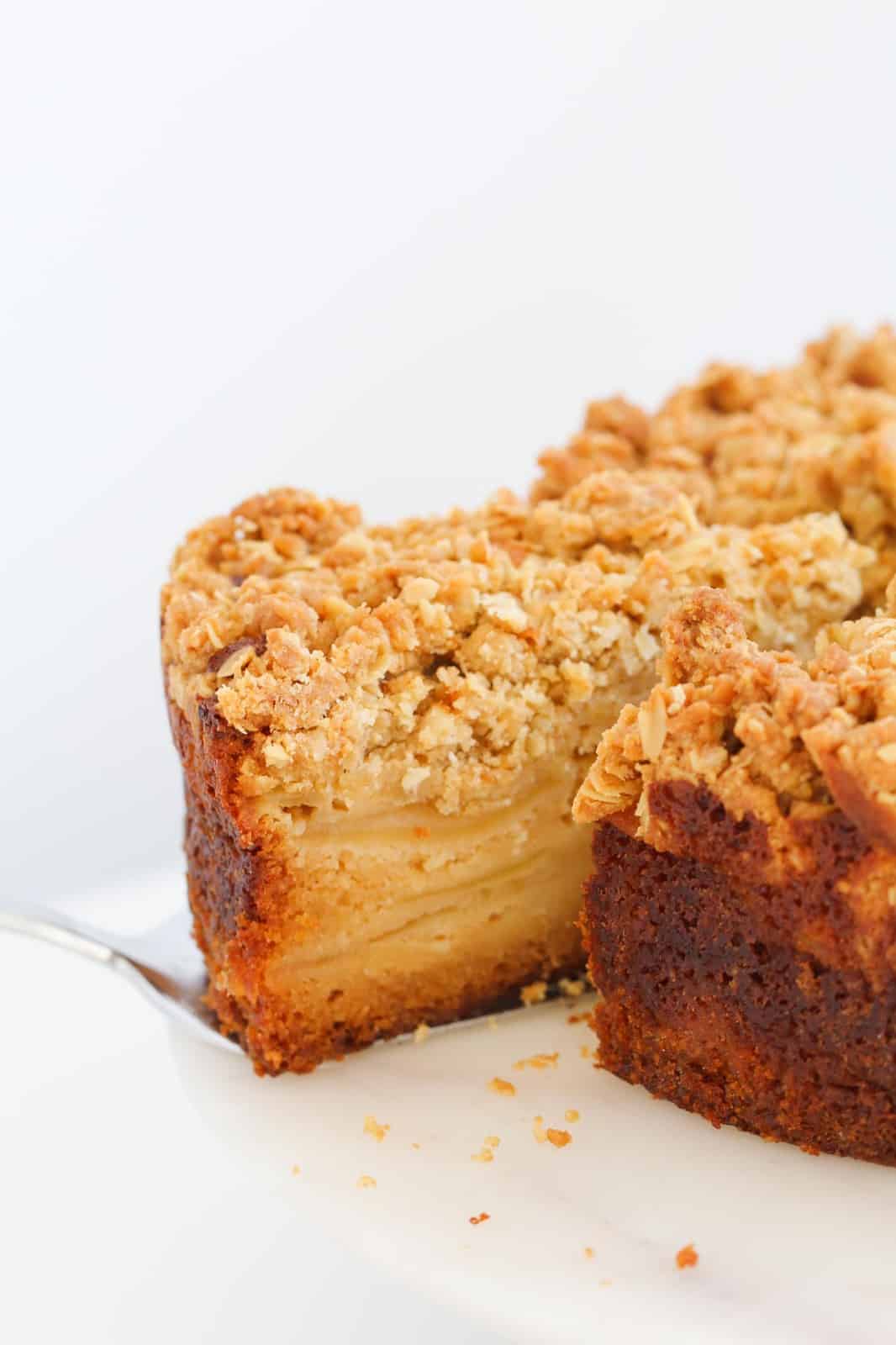 A serve of apple crumble cake being removed from the rest of the cake, showing layers of apple inside